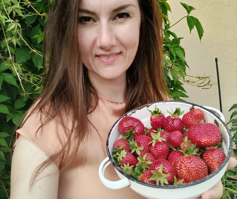 Žena drží misku plnou čerstvých jahod před zelenou rostlinou.